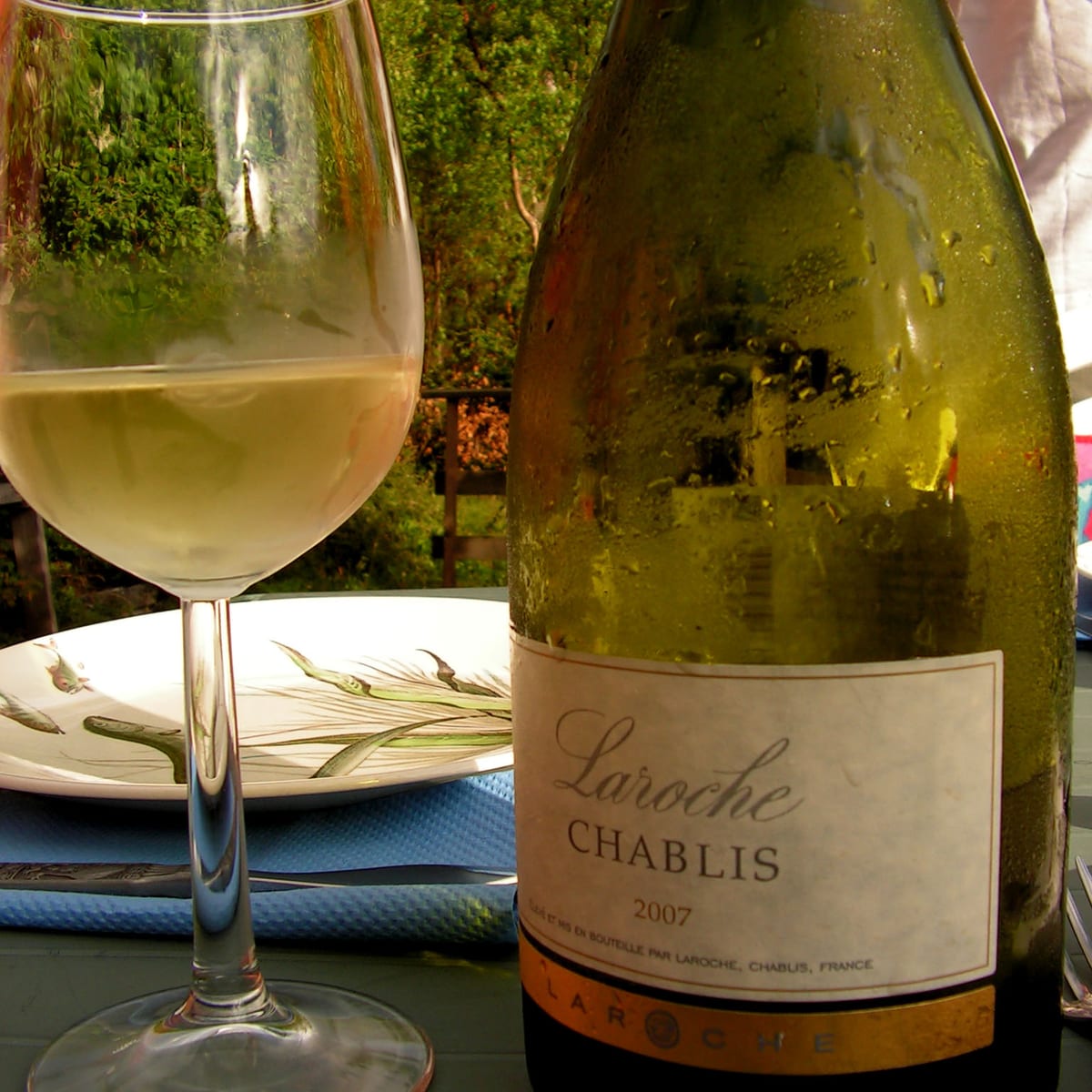 Bouteille de Chablis du domaine Laroche et verre de vin blanc servis en terrasse